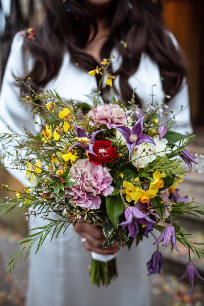 Bride holding a loose bouquet of wildflowers, confetti caught in her hair