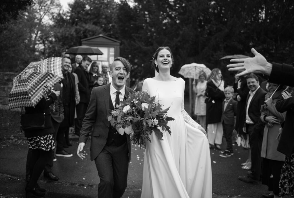 Bride and groom leaving the church through umbrellas and confetti in the rain, black and white photograph