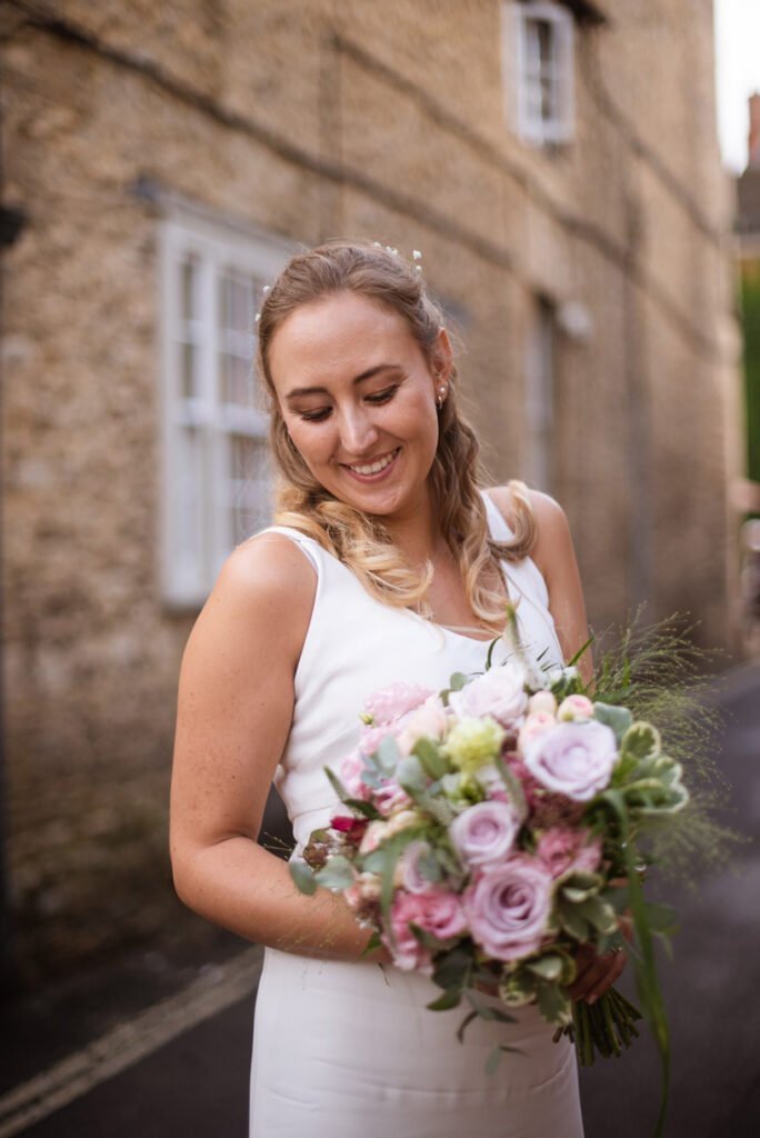 Bride looking down at her pink and cream bouquet against a stone wall