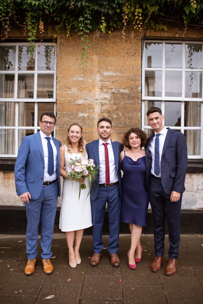 Bride and groom with family lined up outside a Cotswold stone building