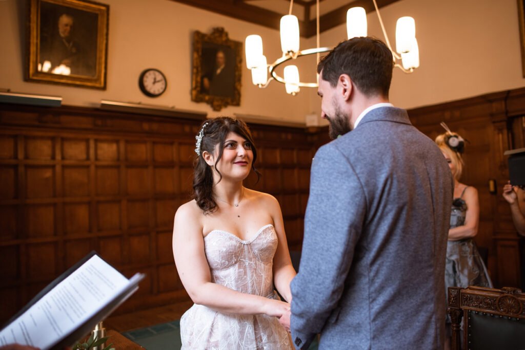 Bride and groom holding hands facing each other in a panelled ceremony room