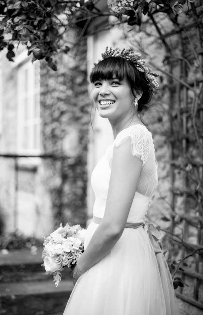 Bride in a flower crown laughing beneath a wisteria arch, black and white photograph