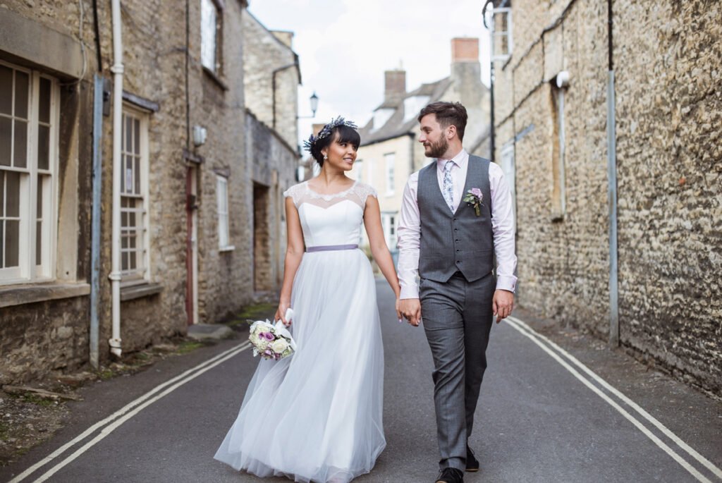 Bride and groom walking hand in hand down a Cotswold stone lane