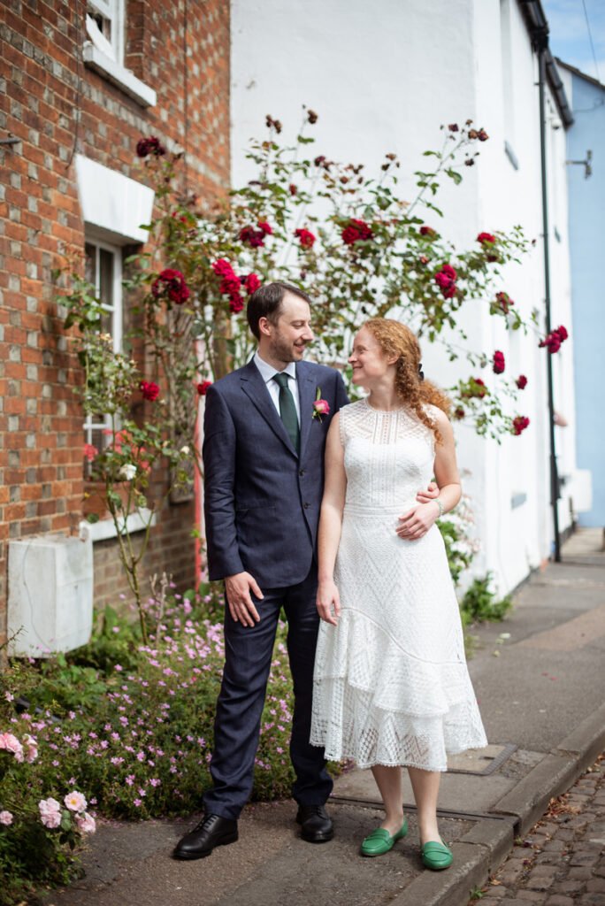 Bride and groom laughing together beneath climbing roses outside a brick cottage