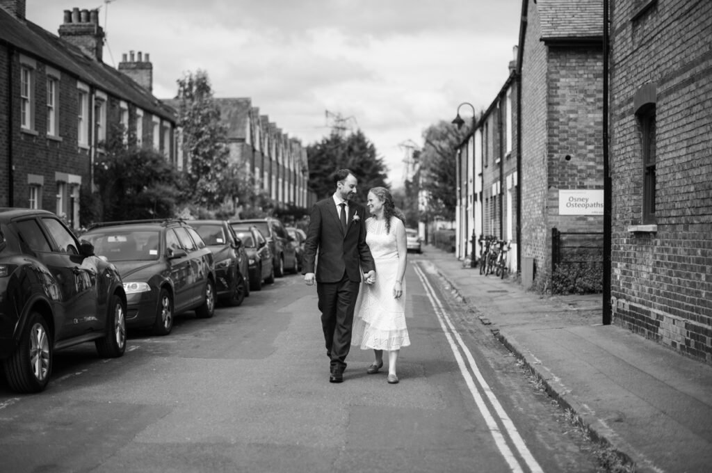 Bride and groom walking a terraced street hand in hand, black and white photograph