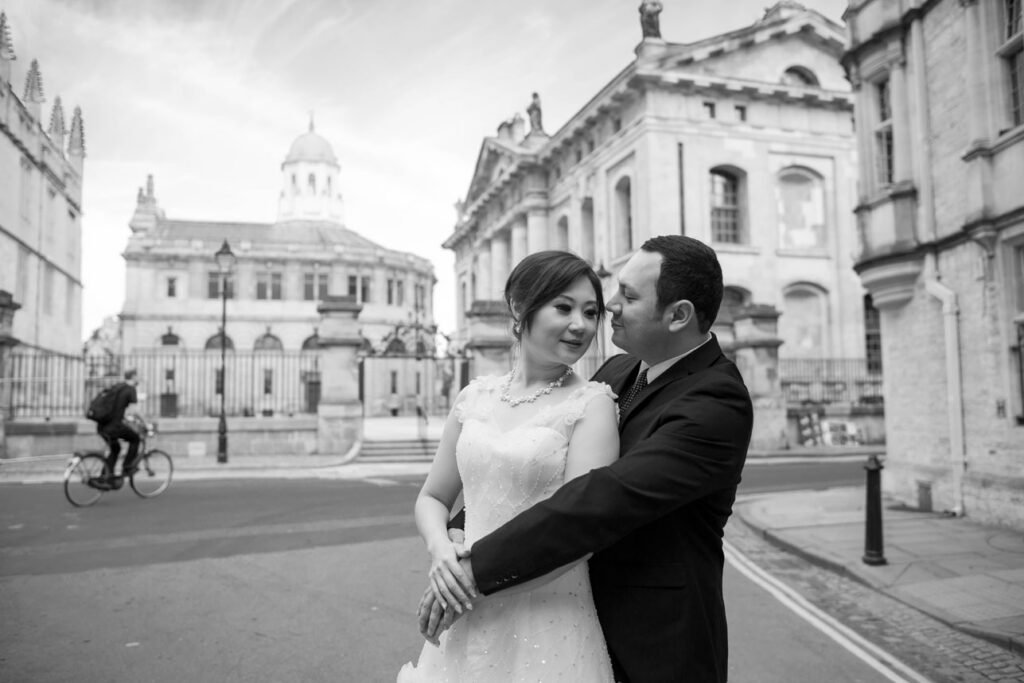 Bride and groom embracing in an Oxford street, the Sheldonian Theatre behind them