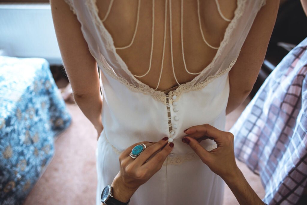 Bridesmaid fastening the buttons at the back of the bride's dress