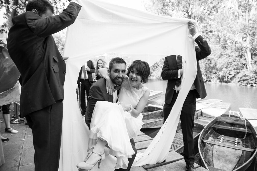 Guests holding a sheet over a bride and groom in a punt, black and white photograph